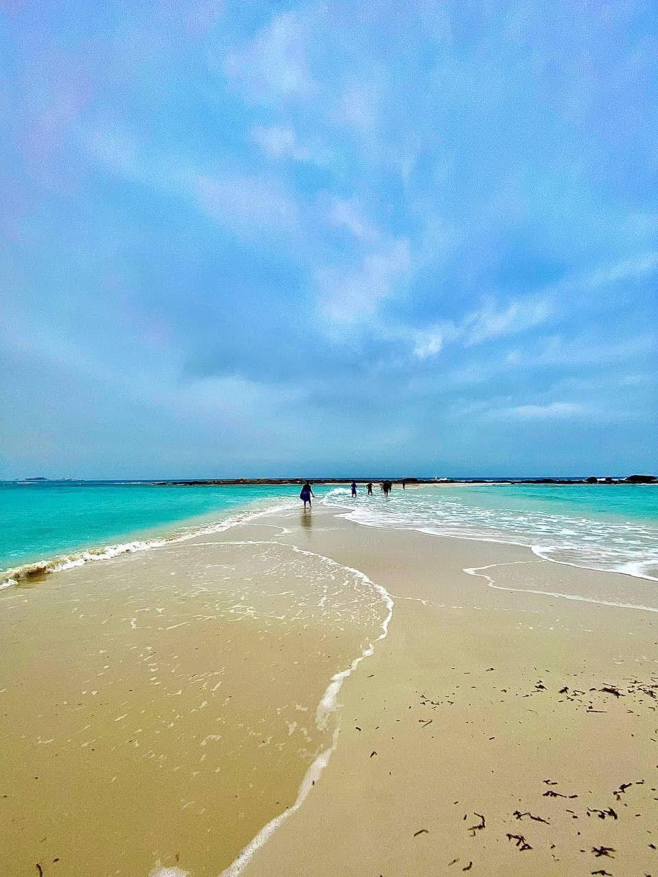 White sand beach with turquoise water, people walking along the shore