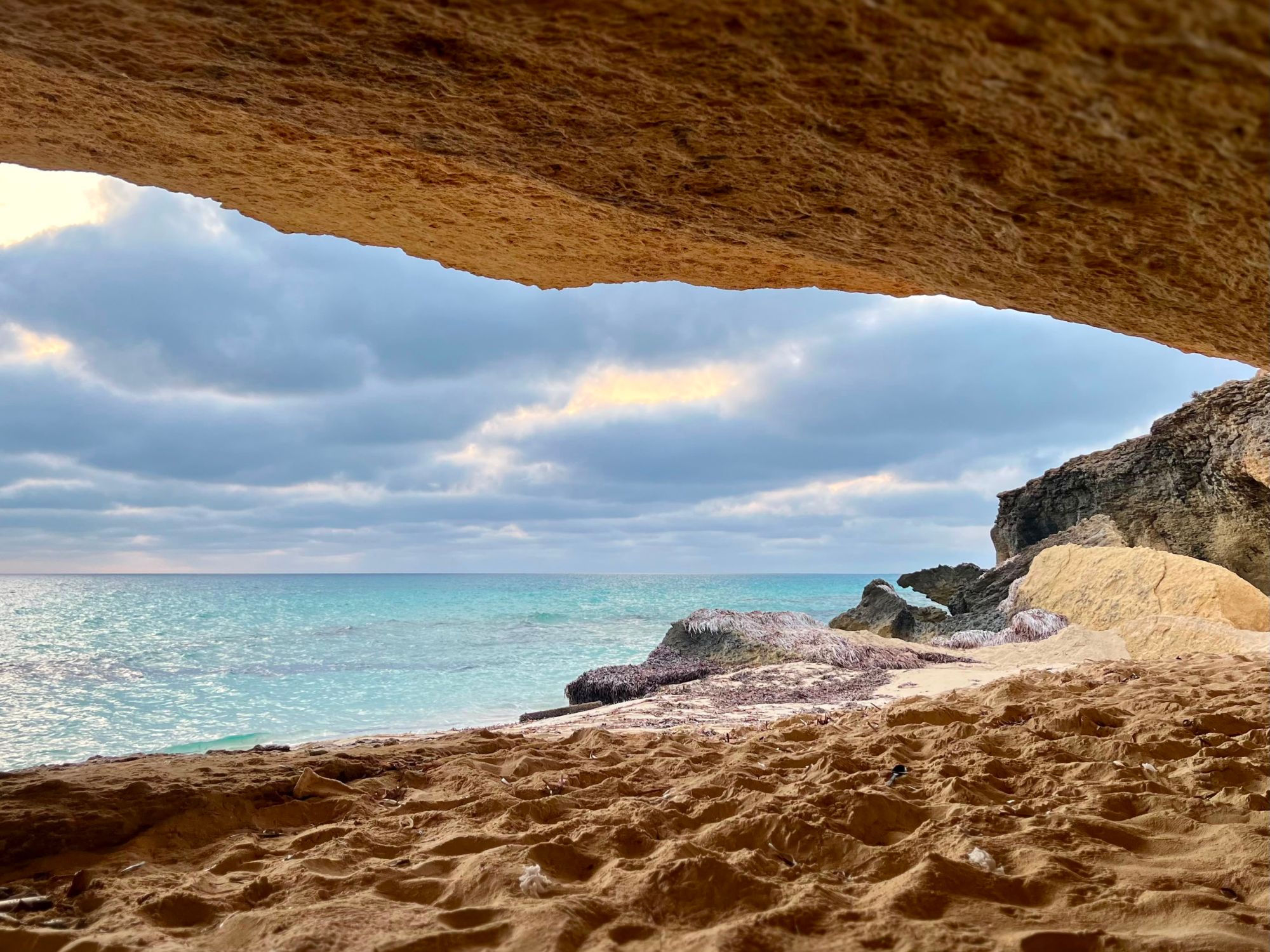 Looking out from inside a golden limestone cave to turquoise water and sandy shore