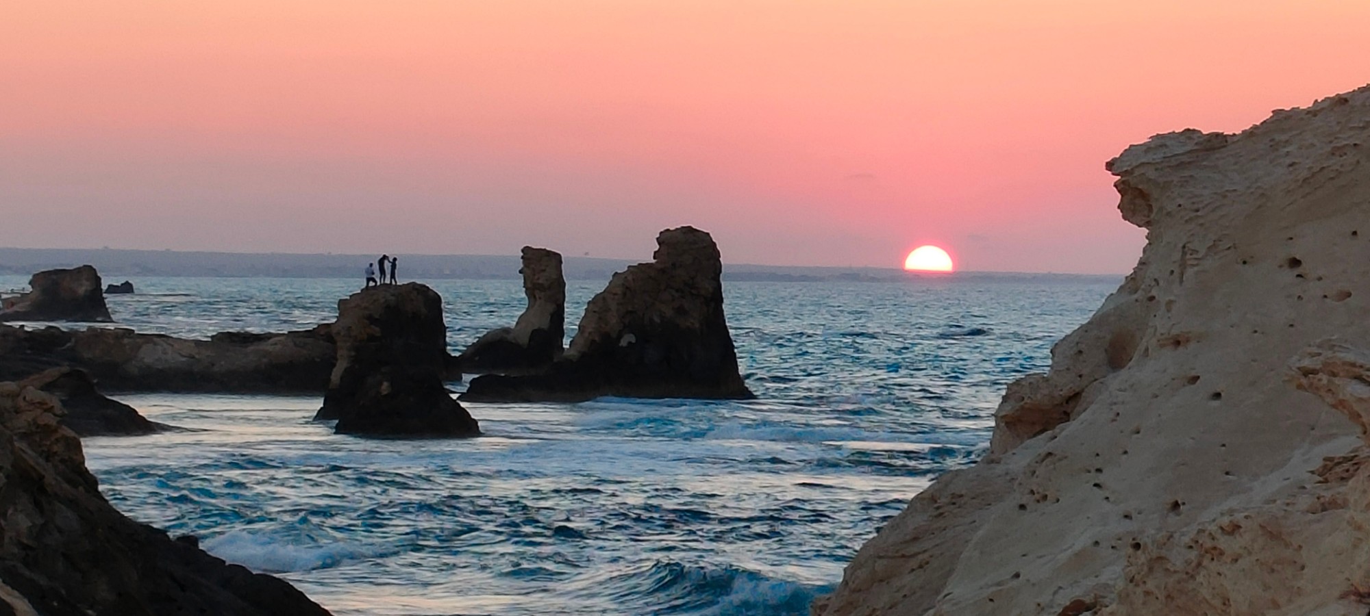Dramatic sunset behind rock pillars at Matahani, silhouettes of people on the rocks